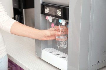 Woman filling glass from water cooler in office © Africa Studio