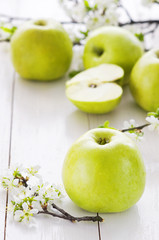 Ripe green apples with spring flowers on a white wooden background.