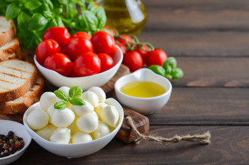 Italian food ingredients – mozzarella, tomatoes, basil and olive oil on rustic wooden table.