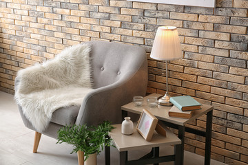 Elegant table lamp and comfortable armchair in room interior near brick wall