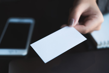Obraz premium Business woman holding and giving business card to someone with mobile phone and notebook on table in office