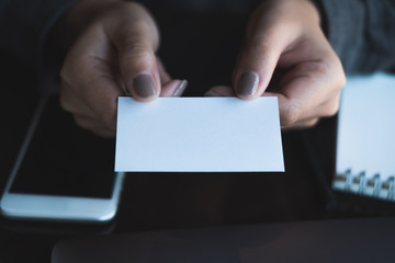 Obraz premium Business woman holding and giving business card to someone with mobile phone and notebook on table in office