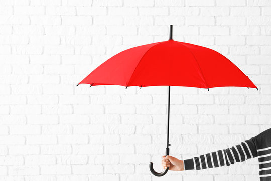 Woman holding stylish red umbrella on brick wall background