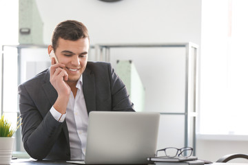 Young man in office wear talking on phone at workplace