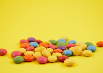 Obraz premium Colorful chocolate lentils candy pile stock photo images. Multicolored round candies on a yellow background. Assorted chocolate lentils stock images
