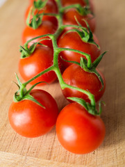 Little branch of cherry tomatoes over wooden background.