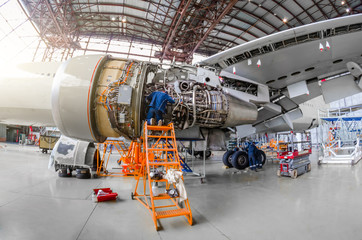 Specialist mechanic repairs the maintenance of a large engine of a passenger aircraft in a hangar. View of engine without bonnet, wing and landing gear. © aapsky