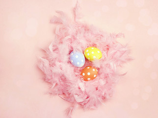 Colored Easter eggs with feathers in the nest on pink background.