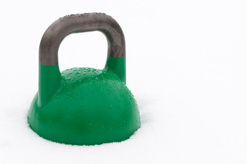 Naklejka na ściany i meble Green competition kettlebell covered with water droplets outside in the snow. Potential copy space to the right of kettlebell. Green competition kettlebells weigh 24kg.