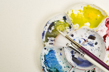Artists flower shaped style watercolour palette and brushes  on a white textured paper background with copy space