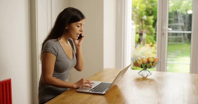 4K Beautiful Hispanic woman working on laptop at home & making a phone call. Slow motion.