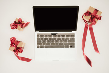 Laptop with blank screen between gift boxes on white surface