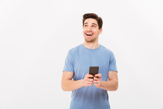 Portrait of beautiful man with short dark hair looking aside and smiling with black cell phone in hand, isolated over white background