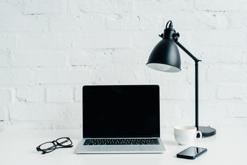 Fototapeta na wymiar Laptop with blank screen, smartphone, lamp and eyeglasses on desk