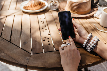 Close up of a women's hands holding cell telephone, hipster girl watching video on mobile phone during coffee break