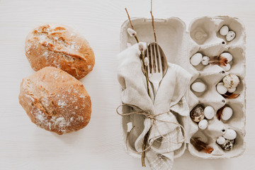 Natural Easter table decoration with silverware in egg box and homemade loaf of bread on white wooden table