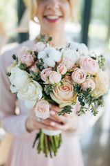 Bridal bouquet with pink roses and white tupils in young bride hands, focus of flowers.  Spring freshness of tulips and roses in one delicate bouquet. 