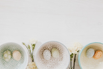 Easter eggs in decorative bowls and gillyflowers on the bottom of white wooden background