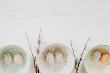 Easter eggs in decorative bowls and fluffy willow on the bottom of white wooden background
