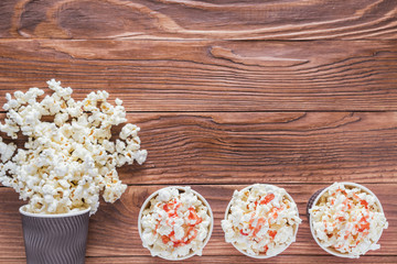 Popcorn in paper cups on a rustic wooden background with copy space, top view, flat lay. Cinema concept. Sweet popcorn with strawberry syrup.