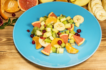 A fresh dietetic fruit and citrus salad is cut on a blue plate. The plate is on a wooden table,...