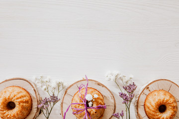Muffins on wooden blocks lying on wooden table with violet and white flowers, flat lay