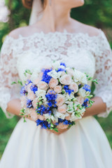 Wedding bouquet in hands of the bride against the background of greenery in the park. Closeup.
