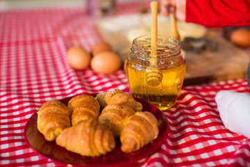 fresh baked croissant with jar of honey, on red tablecloth in the kitchen
