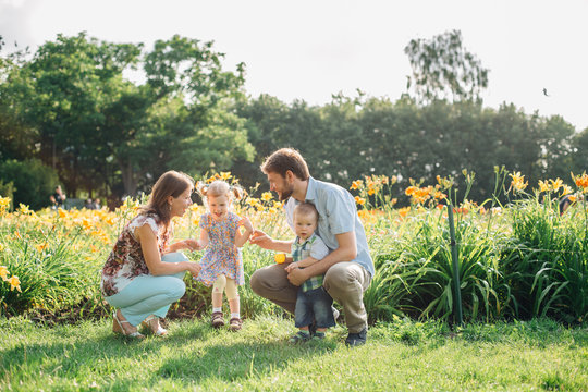 Young happy family having fun in flowers outdoors. Couple in love holding their cute children. Mother father daughter son.