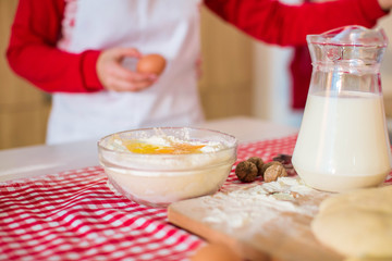 Egg in plate with white flour. Preparation of dough for dessert. Pitcher with fresh milk