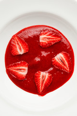 frontal shot pieces of strawberries on berry jam in white plate. background for tasty and colorful dessert.