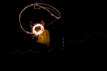 A young woman playing with sparklers at night creating a circular lasso.