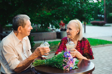 Happy elderly couple in love drinking lemonade in a cafe on the street
