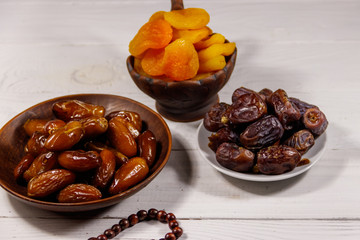 Dried apricots and dates fruit with wooden rosary on white wooden table