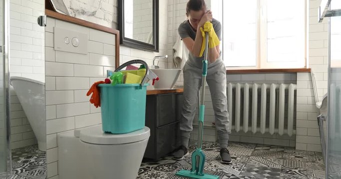 Woman is tired to cleaning tile in toilet. Woman holding a mop and cleaning floor in bathroom