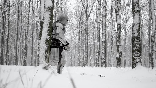 Brave warrior wearing steel armor and helmet walking through winter snowy wood to battlefield in slow motion. Reconstruction of historical times