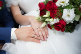 Wedding rings on the fingers of the bride and groom on the background of a wedding bouquet. Closeup.