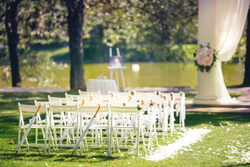  Wedding ceremony decoration with chairs and arch near the lake. Outdoor wedding ceremony at summer park 