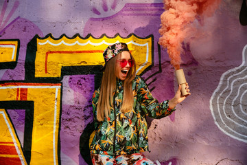 Funny girl with colored smoke bomb standing near the wall with drawing