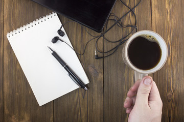 Laptop headphones, notebook, cup of coffee and hand, wooden background
