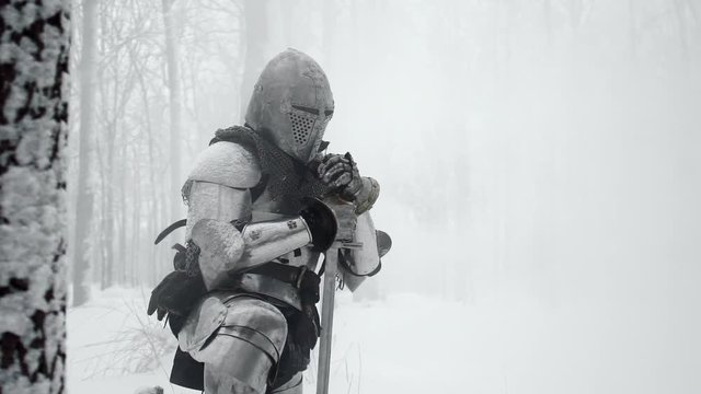 Portrait of medieval warrior armed with steel weapon standing on one knee on winter nature, in slow motion. Reconstruction of ancient times