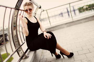 Beautiful fashionable blonde girl in black dress and wearing sunglasses. Open space.