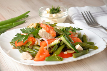 Spring salad of chicken breast, mushrooms, black-eyed peas, cucumbers, tomatoes and onions on a white plate. Healthy food. Close-up view.