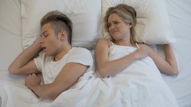 Annoyed woman closing ears while man snoring loudly in bed, apnea disease