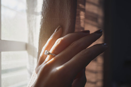 Close up of elegant diamond ring on woman finger with window and sunlight tone background. (soft and selective focus) Wedding and love concept.