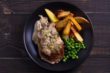 Beef steak with mushroom cream sauce, potato wedges  and green peas. View from above, top