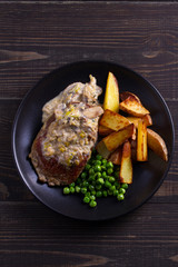 Beef steak with mushroom cream sauce, potato wedges  and green peas. View from above, top