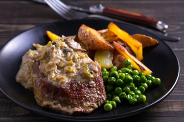 Beef steak with mushroom cream sauce, potato wedges  and green peas