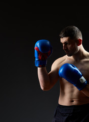 Fototapeta na wymiar Low key studio portrait of handsome muscular fighter practicing boxing on dark blurred background