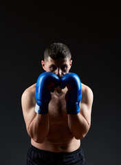 Low key studio portrait of handsome muscular fighter practicing boxing on dark blurred background